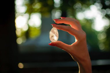 Vumfit, imbuilding veya meditasyon için şeffaf ametist kuvars yoni yumurta ile Kadın el. Gökyüzü ve gündoğumu arka plan açık havada ellerde parlayan kristal yumurta. Kadın sağlığı kavramı.