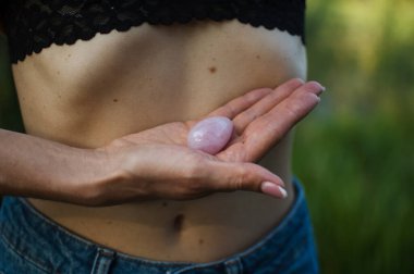 Yetişkin bir kadın çıplak karnının üzerinde vumfit, imbuilding ya da meditasyon için pembe kuvars yumurtası tutuyor. Kadın sağlığı kavramı