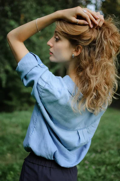 Voltar ver retrato de menina loira sexy com cabelo encaracolado vestindo azul casual jeans blusa posando no parque em árvores verdes fundo. Conceito de estilo Hipster . — Fotografia de Stock