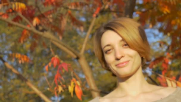 短いブロンドの髪の若い女の子は、赤とオレンジの葉の背景に秋の晴れた日に屋外で竹の歯ブラシを保持しています。環境配慮と廃棄物ゼロのコンセプト — ストック動画