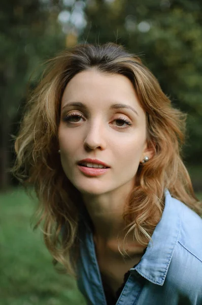 Menina loira vestindo azul casual jeans blusa está olhando para a câmera no parque em árvores verdes fundo — Fotografia de Stock