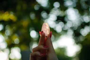 Vumfit, imbuilding veya meditasyon için şeffaf ametist kuvars yoni yumurta ile Kadın el. Gökyüzü ve gündoğumu arka plan açık havada ellerde parlayan kristal yumurta. Kadın sağlığı kavramı.