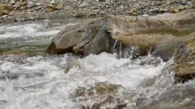 Büyük gri taşlar ve hızlı su ile şeffaf dağ deresinin yakın çekim videosu.