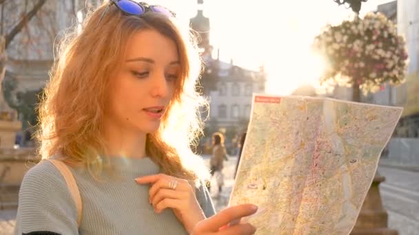 Adult girl is looking at the paper map and searching for direction early in the ancient European city on empty square, tourism concept — стоковое видео