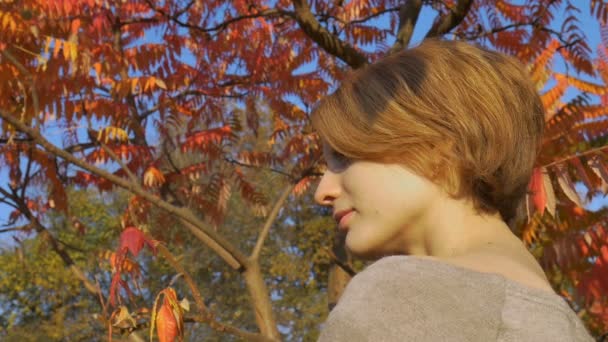 Chica joven con el pelo corto y rubio está sosteniendo un cepillo de dientes de bambú al aire libre durante el clima soleado en otoño sobre fondo de hojas rojas y naranjas. Adecuación al medio ambiente y concepto cero residuos — Vídeos de Stock