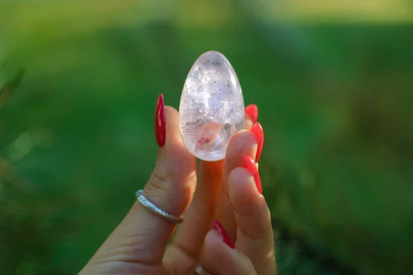 Mano femminile con uovo di yoni di quarzo ametista trasparente per vumfit, imbuilding o meditazione. Uovo di cristallo lucente in mani su cielo e sfondo di alba all'aperto. Concetto di salute delle donne . — Foto Stock