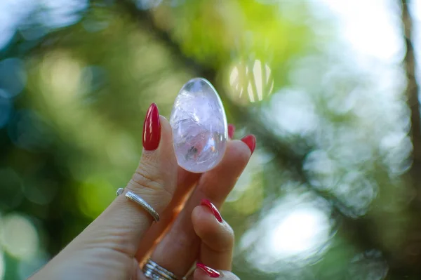 Female hand with transparent amethyst quartz yoni egg for vumfit, imbuilding or meditation. Shining crystal egg in hands on sky and sunrise background outdoors. Womens health concept.