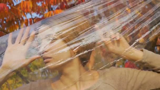 Outdoors portrait of pretty woman with short blonde hair looking through a plastic bag, the girl cant breathe because of the polyethylene wrap. Human responsibility, world environment day — Stock Video