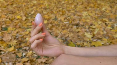 Turuncu manikürlü kadın eli, sonbahar günü açık havada düşen sarı yapraklar üzerinde vumfit, imbuilding veya meditasyon için pembe kuvars yumurtası tutuyor.