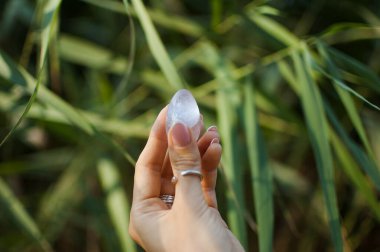 Vumfit, imbuilding veya meditasyon için şeffaf menekşe ametist yoni yumurta tutan Fransız manikür ile Kadın el. Yeşil arka plan açık havada ellerde Kristal kuvars yumurta