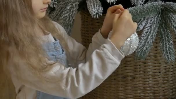 Kleines Mädchen schmückt Weihnachtsbaum mit großen silbernen Kugeln. Nettes blondes Weibchen bereitet sich zu Hause auf Weihnachtsfeier vor. — Stockvideo