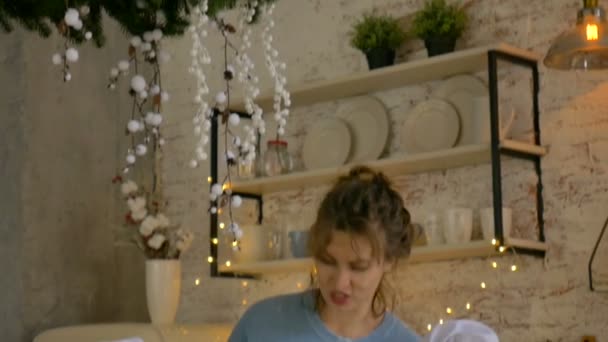 Jovem mãe encaracolado sorridente com seu filho e filha estão cozinhando biscoitos de Natal em casa na cozinha com decoração de Natal . — Vídeo de Stock