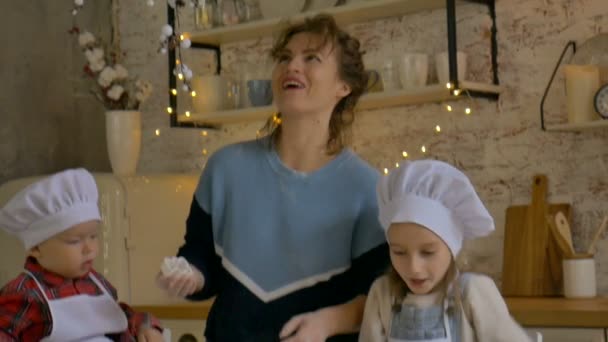 Jonge krullende moeder met haar zoon en dochter koken kerstkoekjes thuis in de keuken met kerstversiering. — Stockvideo