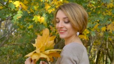 Emotional attractive young woman with blonde short hair and biege dress holding a bouquet of autumn leaves above her head and posing in a beautiful park outdoors