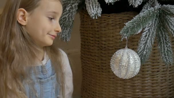 Young girl is helping with decorating the Christmas tree, holding some Xmas silver bauble in her hand, happy childhood and holliday concepts — Stock Video