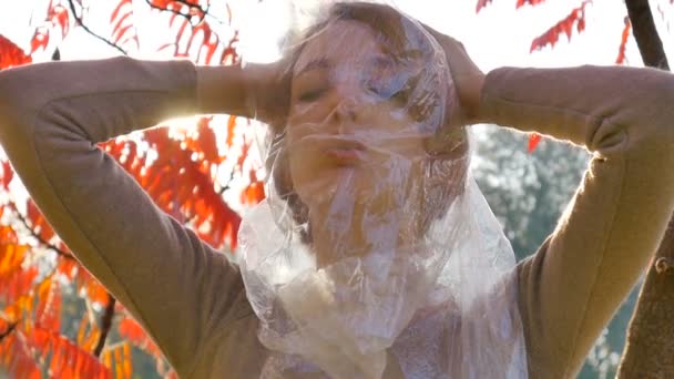 Hübsche Frau mit kurzen blonden Haaren, die durch eine Plastiktüte schaut, das Mädchen kann wegen der Polyethylenfolie nicht atmen. Lungenhochdruck, Asthma, Pneumothorax-Konzept — Stockvideo