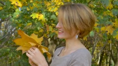 Emotional attractive young woman with blonde short hair and biege dress holding a bouquet of autumn leaves above her head and posing in a beautiful park outdoors