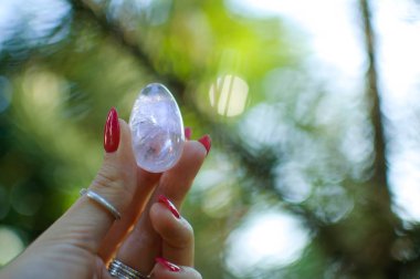 Vumfit, imbuilding veya meditasyon için şeffaf ametist kuvars yoni yumurta ile Kadın el. Gökyüzü ve gündoğumu arka plan açık havada ellerde parlayan kristal yumurta. Kadın sağlığı kavramı.