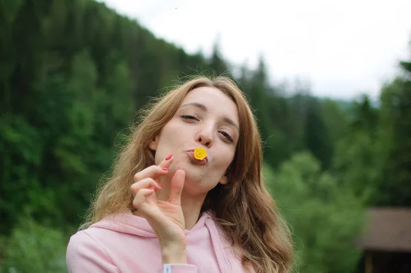 Portrait en plein air de jeune femme blonde calme en vêtements roses avec petite fleur jaune dans la bouche sur la colline avec fond de forêt verte au printemps ou au début de l'automne dans les montagnes — Photo