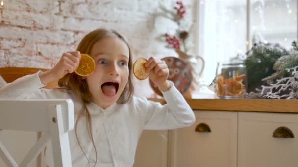 Leende liten blond flicka grimma och täcka sina ögon med torkade apelsinskivor hemma med loft stil och jul dekoration på bakgrunden, god jul koncept — Stockvideo