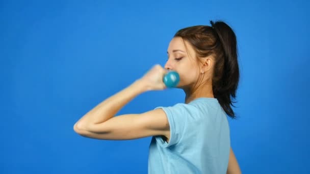 Pretty Young Sports Woman with Dumbbell in Hand Making Her Exercise at Blue Studio Background (en inglés). Chica bonita con cola de caballo en Fitwear. Concepto de culturismo . — Vídeo de stock