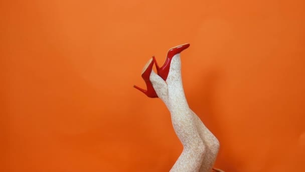 Sexy piernas largas en zapatos de tacón alto rojo y medias de rejilla blanca sobre fondo naranja. Estilo retro — Vídeos de Stock