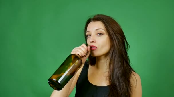 Χαριτωμένο μεθυσμένος κορίτσι με μακριά μαλλιά πίνει κρασί από σκούρο μπουκάλι σε πράσινο φόντο στο στούντιο — Αρχείο Βίντεο