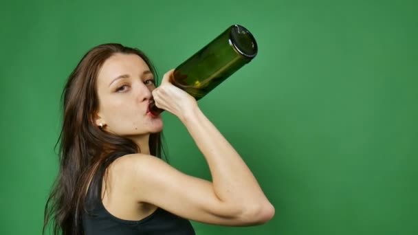 Jeune femme brune boit du vin de bouteille sombre sur fond vert en studio — Video