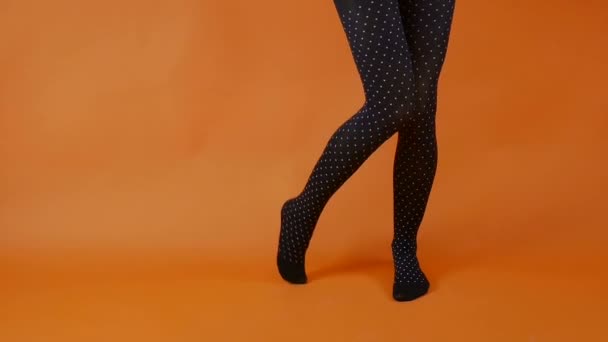 Bas noirs sur des jambes de femme parfaites sur fond orange vif, modèle féminin danse en studio — Video