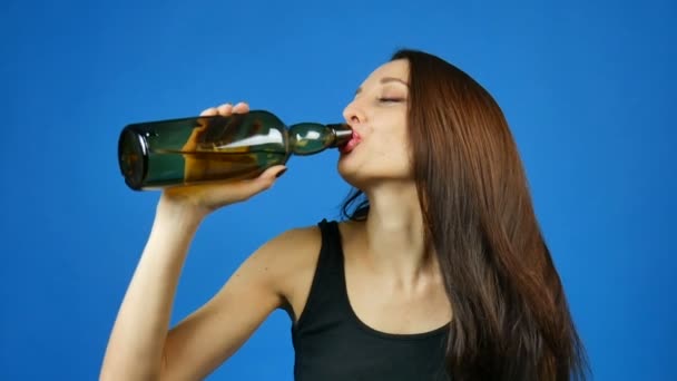 Joven morena bebiendo vino de botella verde oscuro sobre fondo azul en estudio — Vídeos de Stock