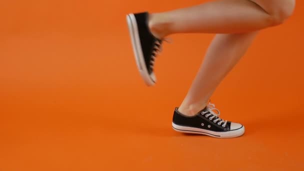 Las piernas femeninas en zapatillas blancas y negras están bailando sobre un fondo brillante en el estudio. Zapatos clásicos. Vida sana, personas activas . — Vídeo de stock