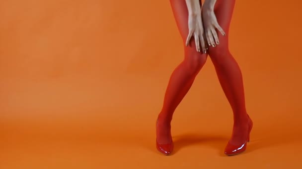 Női modell tökéletes hosszú lábak piros harisnya és sarok dombok sétál a stúdióban több mint világos narancs háttér — Stock videók