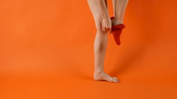 Female model with perfect long legs is wearing red tights on in studio over bright orange background — Stock Video