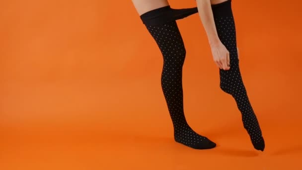 Female model with perfect long legs is wearing black tights on in studio over bright orange background