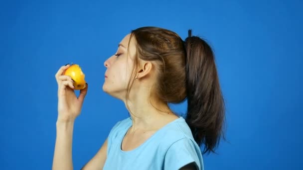 Χαμογελώντας γυναίκα με υγιή δόντια τρώει κόκκινο μήλο σε μπλε φόντο στο στούντιο. Έννοια δίαιτας. Χορτοφαγικά τρόφιμα. — Αρχείο Βίντεο