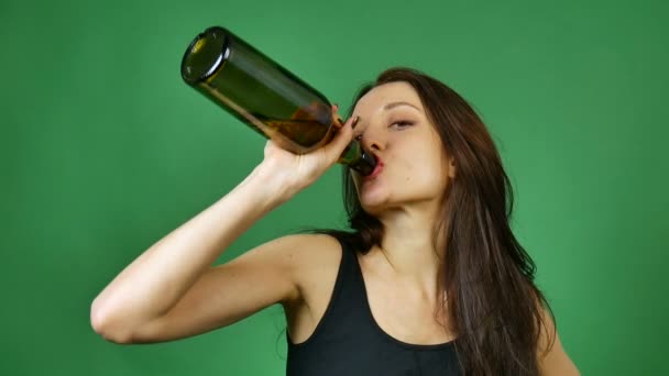 Junge brünette Frau trinkt Wein aus dunkler Flasche auf grünem Hintergrund im Studio — Stockvideo