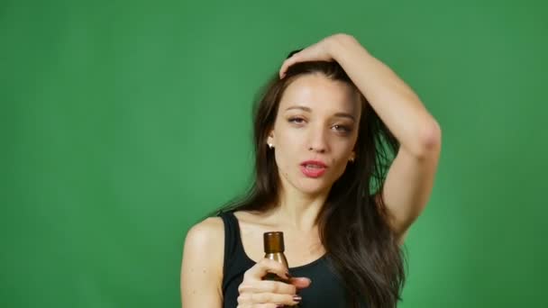 Ridere ragazza ubriaca con i capelli lunghi sta bevendo vino da bottiglia scura su sfondo verde in studio — Video Stock