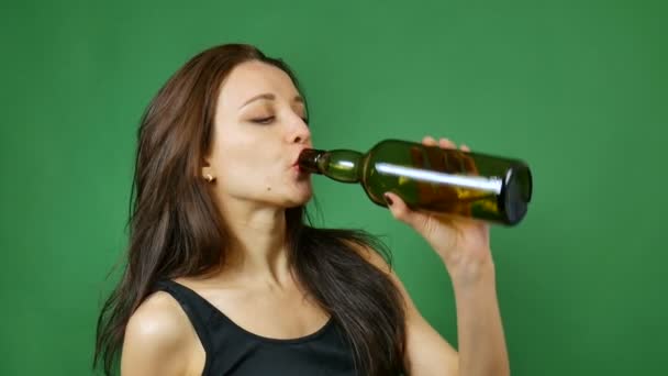 Junge brünette Frau trinkt Wein aus dunkler Flasche auf grünem Hintergrund im Studio — Stockvideo