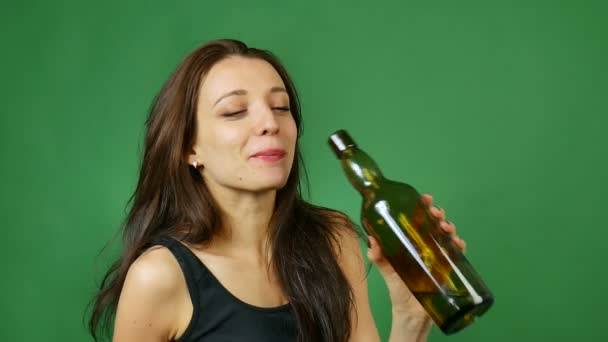 Skrattar full flicka med långt hår dricker vin från mörk flaska på grön bakgrund i studio — Stockvideo