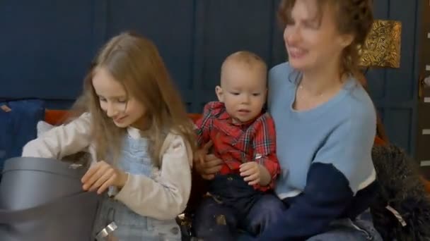 Jonge moeder, dochter en zoon vieren een vakantie of verjaardag met confetti thuis zittend op de oranje bank op donkerblauwe muurachtergrond — Stockvideo