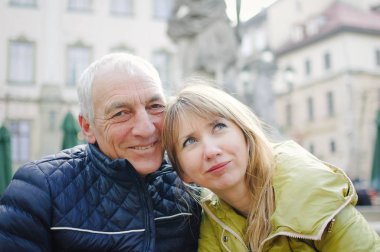 Yakışıklı yaşlı adam, genç sarışın karısını kucaklıyor. Baharın başında ya da sonbaharda antik şehirde birlikte vakit geçiriyorlar..