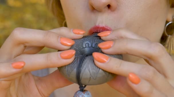 Close-up ao ar livre vídeo de jovem xamã do sexo feminino tocando no instrumento tradicional de cerâmica ocarina segurando-o em suas mãos com manicure laranja na floresta durante o outono — Vídeo de Stock