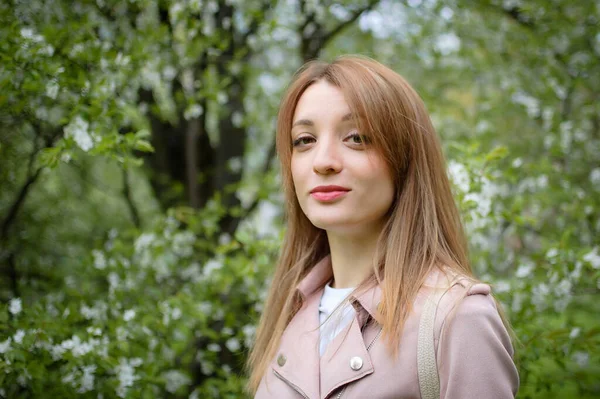 Joven mujer bonita con un pelo rubio posando cerca de un gran árbol floreciente en un parque de primavera, retrato femenino al aire libre —  Fotos de Stock