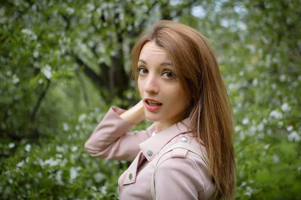 在春天的公园里，一位金发碧眼的年轻漂亮的女士站在一棵盛开的大树旁，在户外的女性画像上 — 图库照片