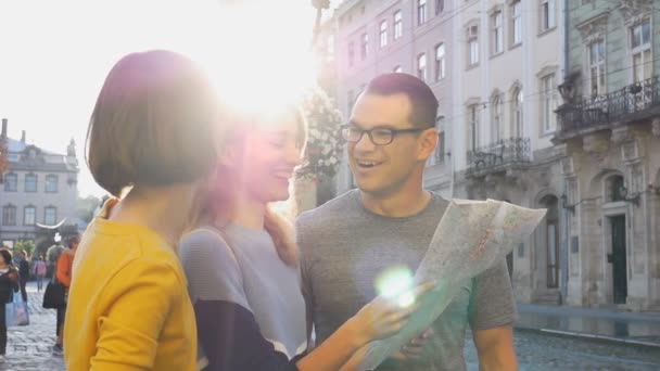 Felices jóvenes turistas sosteniendo un mapa en papel de la antigua ciudad europea temprano en la mañana en la plaza vacía y señalando algún lugar turístico — Vídeos de Stock