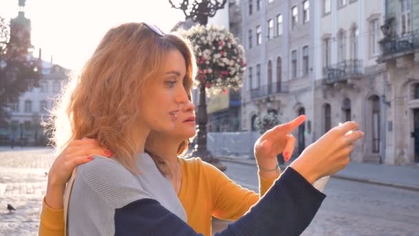 Fröhliche junge Touristen halten frühmorgens eine Papierkarte der antiken europäischen Stadt auf dem leeren Platz und zeigen auf irgendeine Sehenswürdigkeit — Stockvideo