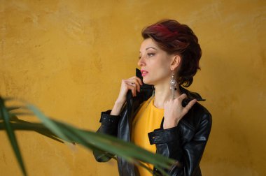Punk rock tarzı parti kıyafetleri içinde göz kamaştırıcı bir kadın. Günlük kıyafetler içinde koyu pembe saçlar, siyah deri ceket ve sarı arka planda uzun küpeler.
