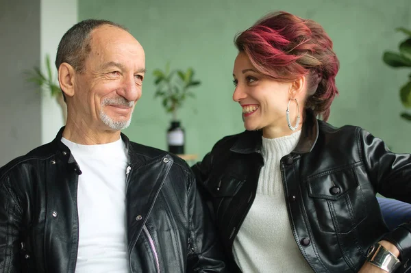 Retrato familiar interior de hija adulta y padre mayor en habitación tipo loft con plantas de interior. Loco hombre y chica con el pelo rosa están usando chaquetas de cuero negro en estilo punk y sonriendo —  Fotos de Stock