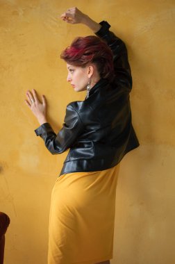 Punk rock tarzı parti kıyafetleri içinde, koyu pembe saçlı, siyah deri ceketli ve sarı arka planda uzun küpeli çekici bir kadın.