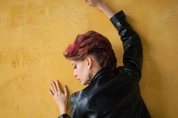 Vista posteriore della signora glamour in stile punk rock abiti da festa con i capelli rosa scuro in abito casual, giacca di pelle nera, e orecchini lunghi su sfondo giallo — Foto Stock
